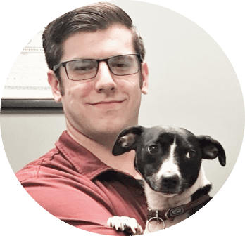 Photo of Andrew Jones holding his dog and smiling at the camera.